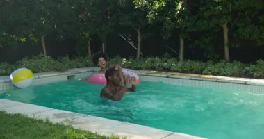 Çeşitli arkadaşlar havuz gününün tadını çıkarıyorlar, kadın şamandırada gülüyor, adam plaj topu atıyor. Boş zaman, yaz tatili, eğlence, arkadaşlık, havuz kenarı, rahatlama.