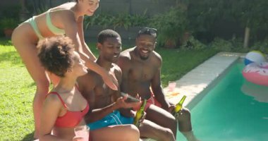 Çeşitli arkadaşlar havuz başında eğleniyor, selfie çekiyor ve yaz güneşinde birlikte gülüyorlar. Tatil, arkadaşlık, eğlence, kahkaha, güneş ışığı, mutluluk