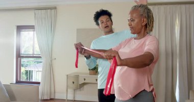 Direniş bandıyla egzersiz yapan, evde bakıcı tarafından desteklenen yaşlı bir kadın. Egzersiz, sağlık, sağlık, bakım, evde bakım, yaşlılık.