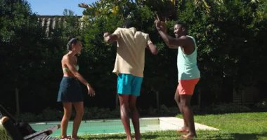 Çeşitli arkadaşlar havuz başında gülüyor ve dans ediyor, güneşli günün tadını birlikte çıkarıyorlar. Tatil, yaz, eğlence, mutluluk, eğlence, kutlamalar