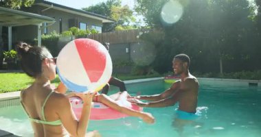 Çeşitli arkadaşlar güneşli bir günde arka bahçede yüzme havuzunda plaj topuyla oynuyorlar. Yaz, tatil, eğlence, su, aktivite, eğlence
