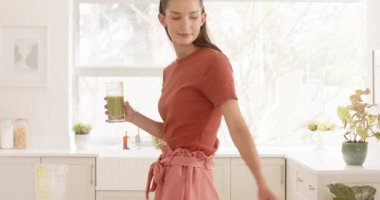 Mutfakta gülümseyen bir kadın sağlıklı meyve suyu hazırlarken akıllı telefon kullanıyor. Yaşam tarzı, sağlık, teknoloji, diyet, beslenme, mutluluk