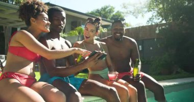 Çeşitli arkadaşlar gülüyor ve havuz kenarında içkilerini paylaşıyorlar, güneşli yaz gününün tadını çıkarıyorlar. Tatil, rahatlama, eğlence, kahkaha, arkadaşlık, açık hava.