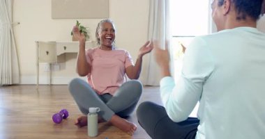 Kıdemli kadın, egzersiz sırasında gülümseyerek ve su şişesini tutarak yerde oturuyor. Fitness, hidrasyon, sağlık, sağlıklı yaşam tarzı, rahatlama, aktif