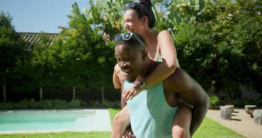 Güneşli arka bahçede havuz başında sırtımda gezintiyle gülen farklı arkadaşlar. Arkadaşlık, boş zaman, yaz, açık hava, bağ, eğlence.