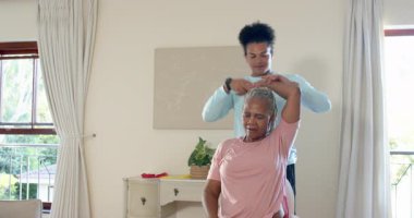 Evde egzersiz yapan yaşlı kadın, bakıcı tarafından sağlıklı yaşam tarzı için destekleniyor. Fitness, refah, bakım, egzersiz, evde çalışma, yaşlılık