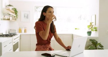 Parlak mutfakta dizüstü bilgisayar kullanan bir kadın, evde odaklanarak çalışıyor. Uzaktan çalışma, telekomünikasyon, üretkenlik, teknoloji, yaşam tarzı, dijital göçebe