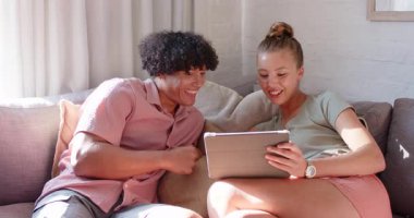 Farklı çiftler kanepede dinleniyor, evde birlikte tablet izlerken gülümsüyorlar. Boş zaman, yaşam tarzı, teknoloji, rahatlama, mutluluk, bağlantı