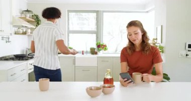 Genç bir kadın mutfakta içki hazırlarken erkekler arka planda, evde yemek pişiriyor. Çeşitli çiftler, ev hayatı, yemek hazırlama, takım çalışması, ev, gündelik