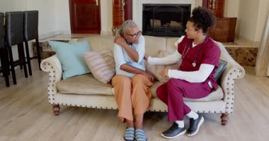 Bakıcı, evde battaniyeli, rahat bir oturma odası ayarlayan yaşlı bir kadına yardım ediyor. Bakım, destek, yaşlılık, yardım, rahatlık, sıcaklık