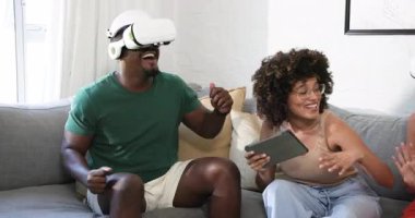 Çeşitli arkadaşlar kanepenin üzerinde sanal gerçeklik oyunlarından zevk alıyorlar, birlikte gülüyorlar ve eğleniyorlar, evde. Eğlence, oyun, teknoloji, aktivite, bağ, eğlence