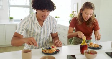 Mutfak masasında pekmezli ve meyveli kahvaltı kreplerinin tadını çıkaran çeşitli çiftler. Beraberlik, aşçılık, ev içi, yemek, konfor, evcil