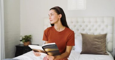 Genç bir kadın yatakta oturmuş kitap okuyor, evinde huzurlu bir anın tadını çıkarıyor. Rahatlama, rahatlama, sükunet, edebiyat, yalnızlık, farkındalık.