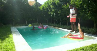 Çeşitli arkadaşlar havuz başında güneşli bir günün tadını çıkarıyorlar, ellerinde içkilerle şamandıralarda dinleniyorlar. Tatil, tatil, yaz, havuz kenarı, dinlenme, yüzme.