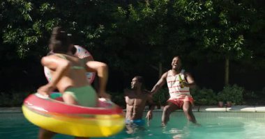 Çeşitli arkadaşlar güneşli bir günde renkli şişme bebeklerle havuzda gülüp sıçrıyor. Havuz partisi, yaz, eğlence, eğlence, tatil, yüzme