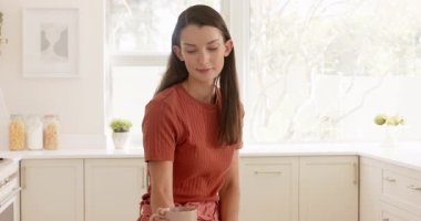 Mutfakta akıllı telefon kullanan, gülümseyen ve sabah kahvesinin tadını çıkaran bir kadın. Teknoloji, kahvaltı, yaşam tarzı, mutluluk, içecek, gündelik