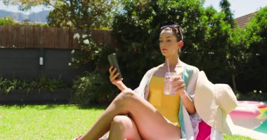 Havuz başında dinlenen, mayo giymiş içki içen, açık havada akıllı telefon kullanan, fotokopi çeken bir kadın. Tatil, dinlenme, rahatlama, teknoloji, yüzme, ferahlama