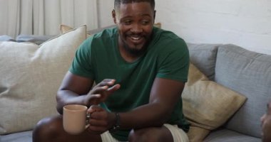 Adam elinde kahve fincanı tutarak kanepede dinleniyor, gülümsüyor ve evde sohbetten zevk alıyor. Rahatlık, rahatlık, rahatlık, rahatlık, mutluluk, iletişim