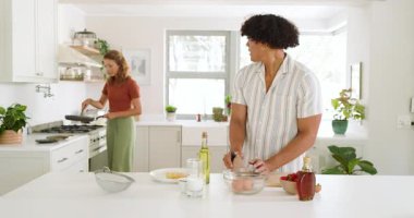 Genç adam mutfakta taze meyve salatası hazırlarken kadınlar evde yemek yapıyor. Mutfak, yemek hazırlama, takım çalışması, sağlıklı, yaşam tarzı, yerli