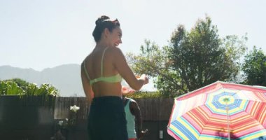 Adam renkli şemsiyeli ve ağaçlı havuz başında güneşli bir günün tadını çıkarıyor. Tatil, dinlenme, dinlenme, güneş, tropikal, açık hava