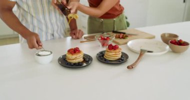 Çeşitli çiftler evlerinde, parlak modern mutfakta çilekli lezzetli krepler hazırlıyorlar. Kahvaltı, yemek pişirme, aşçılık, yaşam tarzı, hazırlık.