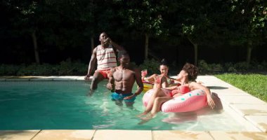 Çeşitli arkadaşlar havuz partisinden zevk alıyorlar, gülüyorlar ve şişme suda içkilerle rahatlıyorlar. Yaz, eğlence, eğlence, rahatlama, yüzme, içecekler