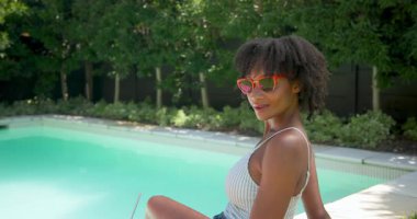 Havuzda dinlenen, güneş gözlüklü bir kadın ferahlatıcı bir içecekle güneşli bir günün tadını çıkarıyor. Tatil, tatil, rahatlama, güneşlenme, ferahlama, açık hava.