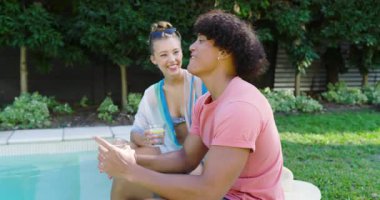 Çeşitli çiftler havuz başında dinleniyor, kadınlar şakacı bir şekilde erkeğin kafasına şapka takıyor, yazın tadını çıkarıyorlar. Tatil, tatil, romantizm, rahatlama, mayo, açık hava.