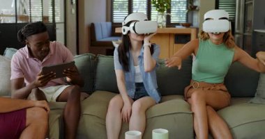 Çeşitli arkadaşlar tableti takip ediyor, işaret ediyor, tepki veriyor ve VR 'ı kanepedeki kulaklıklarla keşfediyorlar. Teknoloji, yenilik, sanal gerçeklik, arkadaşlık, etkileşim, modern, eğlence