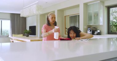 Asyalı anne ve kız mutfakta lekeleri inceliyor, solüsyon püskürtüyor, bez siliyor ve sarılıyor. Aile, bakım, ev, ev, temizlik, yaşam tarzı, etkileşim