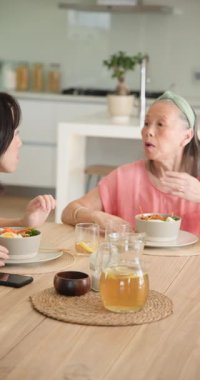 Dikey video: Torununuz evde yemeğin tadını çıkarırken büyükannenize akıllı telefon gösteriyor. Aile, teknoloji, yaşlılar, bağlılık, nesiller arası, paylaşım