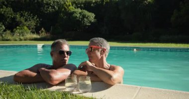 Havuzda rahatlarken, olgun bir çift içkinin ve güneşin tadını çıkarırken, gülümsemelerini paylaşırken. Tatil, tatil, rahatlama, havuz kenarı, mutluluk, içecek.