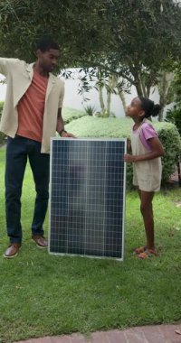 Dikey video: Baba ve çocuk yenilenebilir enerjiyi öğreniyor, arka bahçede güneş panelini inceliyor. Aile, sürdürülebilirlik, teknoloji, eğitim, çevre, yeşil enerji