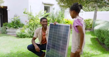 Afrikalı Amerikalı baba ve kız bahçede güneş paneli kuruyor, bahçede güneşli bir günün tadını çıkarıyorlar. Yenilenebilir, enerji, kurulum, sürdürülebilir, bağlanma, teknoloji