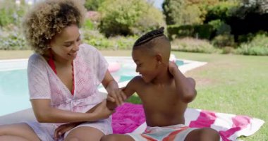 Sıcak güneşe dikkat edin, anne ve okul çağındaki oğlu kollarına ve göğsüne güneş kremi sürüyor. Aile, açık hava, rahatlama, rahatlama, kaynaşma, yaz, canlı