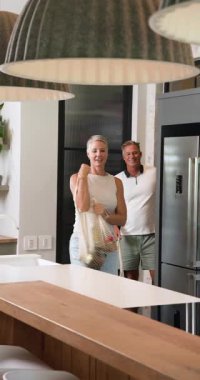 Dikey video: Mutfakta olgun bir çift birlikte yemek hazırlıyor, sohbetten ve kahkahadan zevk alıyor. Yemek pişirme, yemek hazırlama, birliktelik, ilişki, ev hayatı