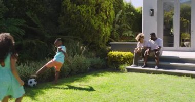 Oğlan bahçeye koşuyor ve kız futbol topu sürüyor. Babam da arka bahçede maça katılmadan önce. Aile, açık hava, eğlence, eğlence, canlı, oyuncu, birliktelik.