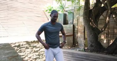 African American man meditating on yoga mat at modern backyard, showing wooden wall and pool. Meditation, tranquility, focus, leisure, relaxation, outdoor, wellness