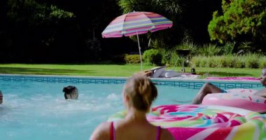 Çeşitli arkadaşlar arka bahçedeki havuza dalan yüzücüleri fark ediyor, su sıçratıyor, el sallıyor ve sohbet ediyorlar. Yaşam tarzı, eğlence, su, açık hava, eğlence, yoldaşlık, hayat dolu.