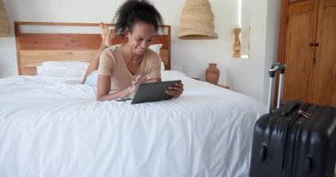 Kadın tablet kullanarak yatakta dinleniyor ve evde gülümsüyor. Teknoloji, eğlence, yaşam tarzı, mutluluk, konfor, rahatlama.