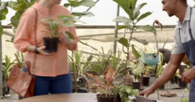 Bahçe kreşindeki serada satılık tabletlerle çeşitli insan ve müşteri arama bitkileri. Bahçe, perakende, teknoloji, alışveriş, bahçıvanlık.