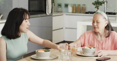 Üst düzey Çinli anne ve kız kadeh kaldırıyor, çay dolduruyor ve mutfaktaki masada salata yiyorlar. Aileler, kaynaşma, beslenme, sıcaklık, gelenek, iletişim, sağlık