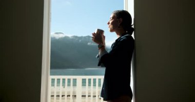 Kadın sabah kahvesini balkonda içiyor, yüzünde güneş ışığını hissediyor, fotokopi çekiyor. Rahatlama, rahatlama, mutluluk, gündoğumu, yaşam tarzı, sükunet