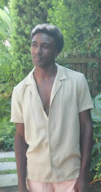 Dikey video: Bahçede genç bir adam yukarı bakıyor, günlük gömlek giyiyor, doğanın tadını çıkarıyor. Açık hava, rahatlama, rahatlama, huzur, huzur, yaşam tarzı.