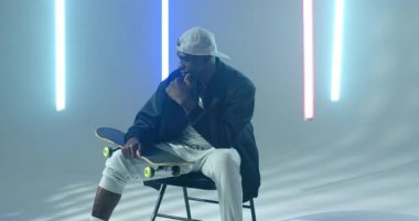 Kucak teftişinde dönen kaykaycı Afrikalı Amerikalı adam stüdyoda mavi LED tüplerle geziyor. Kentsel, yaşam tarzı, modern, minimalist, yansıtıcı, atletik, yaratıcı