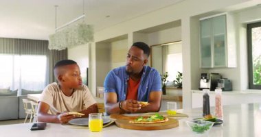 Afrika kökenli Amerikalı baba ve çocuk mutfak adasında pizza topluyor, tatma ve paylaşma yapıyor. Aile, bağ, aşçılık, konfor, yaşam tarzı, erdem, beslenme