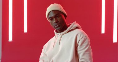 Kırmızı stüdyoya yaslanan Afro-Amerikan adam kapüşonlu ve bereli kıyafetlerini dumana uygun hale getiriyor. Portre, tefekkür, karamsar, sokak giyimi, kentsel, sinematik, içsel