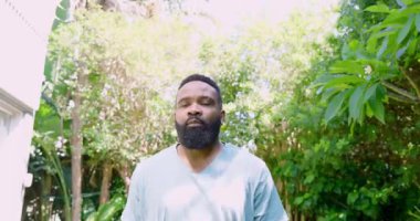 Afro-Amerikalı bir adam açık havada kameraya bakıyor. Yeşilliklerin arasında ciddi bir odak noktası var. Portre, yeşillik, doğa, açık hava, kararlılık, erkeklik, odaklanma