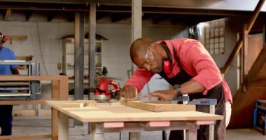 After clamping frame, African American man in red apron sanding edges for smooth finish in workshop. Woodworking, craftsmanship, manual, workshop, tools, industrial, focus