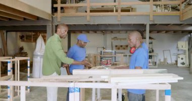 Afro-Amerikan takımı atölyeye giriyor ve tablet vasıtasıyla ahşap kalasları düzenliyor. Sanatçılık, takım çalışması, endüstriyel, ahşap işçiliği, profesyonellik, işbirliği, modern
